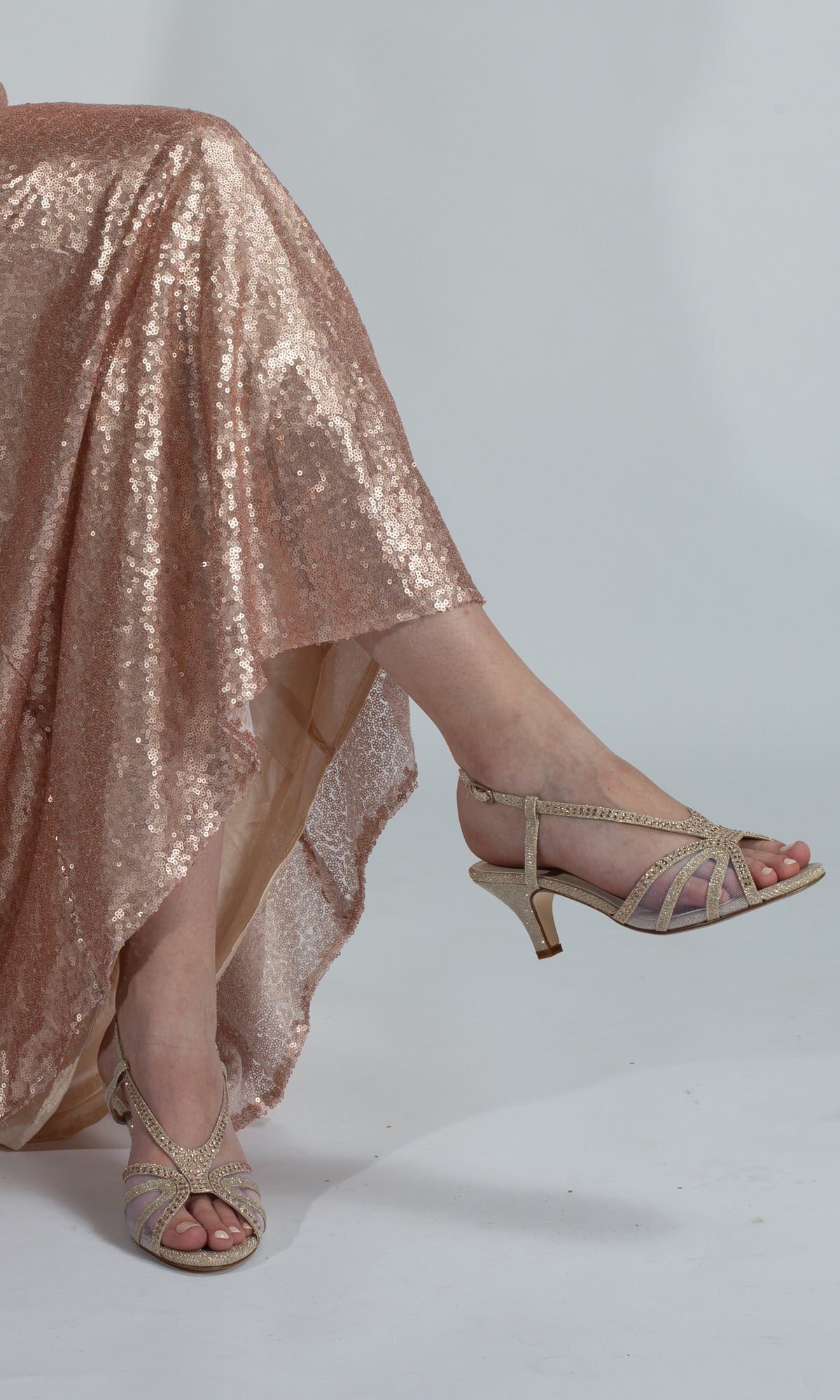 A person in a sparkling rose gold sequin dress and Clara Champagne 1.75in Heel Prom Shoes 4487 sits with crossed legs against a plain background.